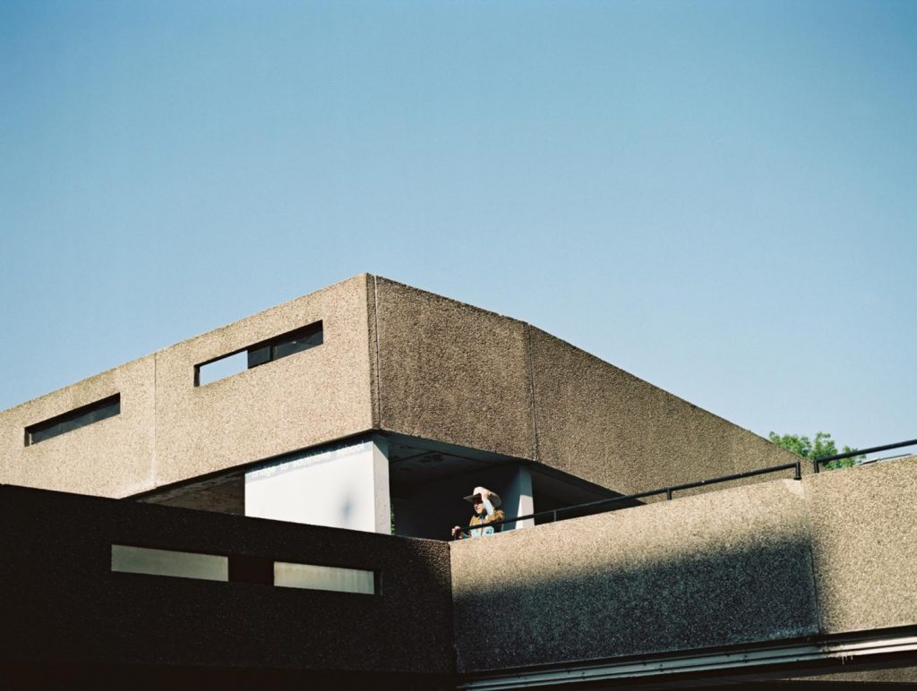 An image of the brutalist Thamesmead estate. A man with a cowboy hat stands on one of the concrete walkways.