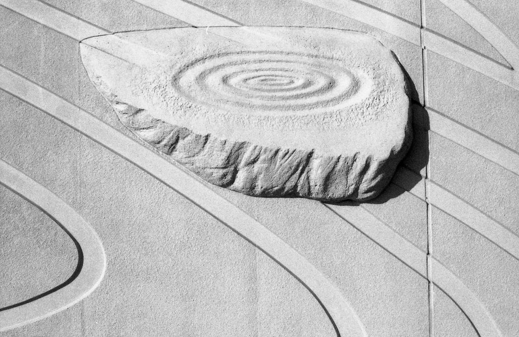 A black and white photo of a sculptural wall with a spriral carved into it