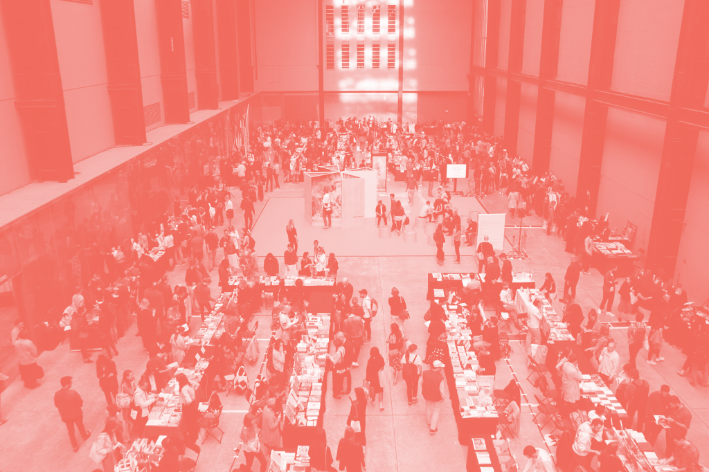 A birds eye view of Offprint publishers' fair in Tate Modern's Turbine Hall. Book stalls are surrounded by crowds of people.