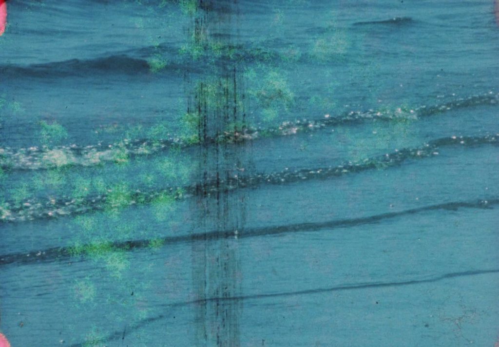 A scratched 16mm frame of the sea, overpainted and dicoloured with green blotches