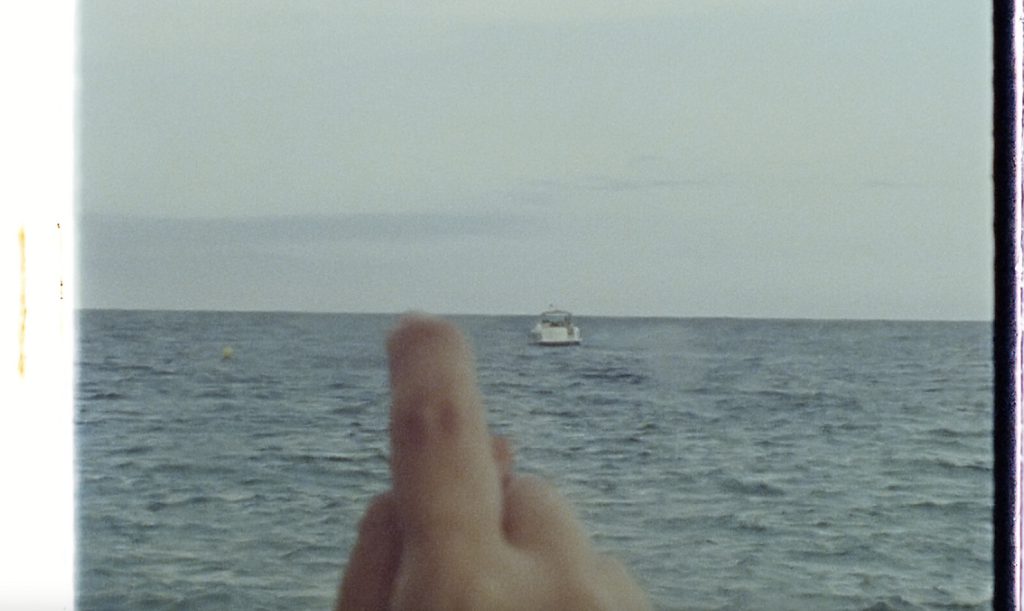 Still from a 16 mm film, a finger traces the horizon line of the sea