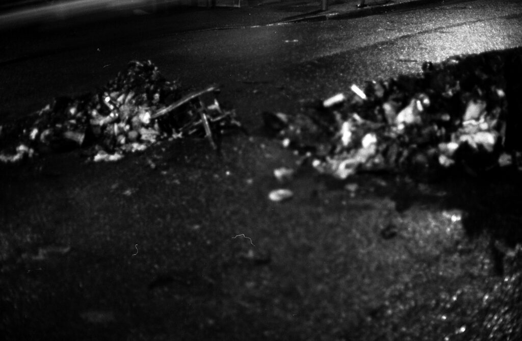 A black and white photo of pile of rubbish burning on a road at night